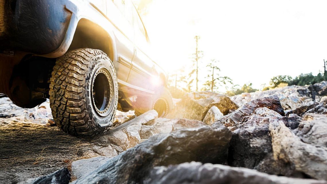 Close-up of an off-road vehicle tire climbing over rocks in rugged terrain, with natural lighting in the background