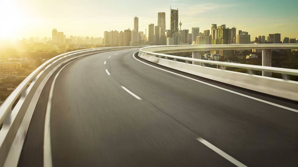 Curved elevated highway leading to a modern urban skyline at sunset, with skyscrapers and a clear sky
